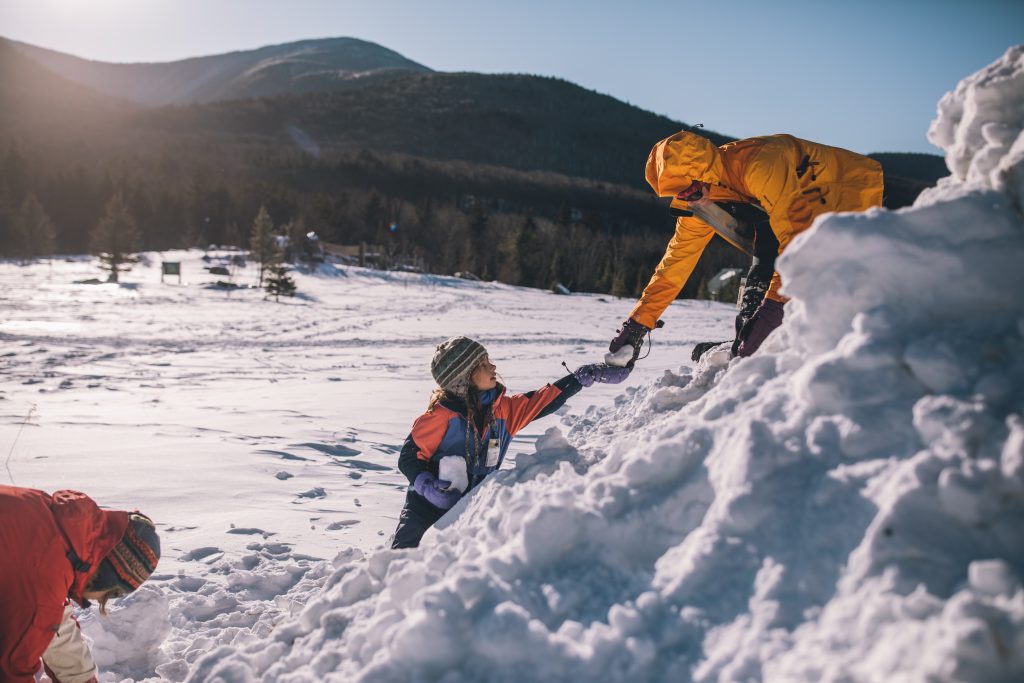 A kid and an adult wearing snow gear play in the snow together.