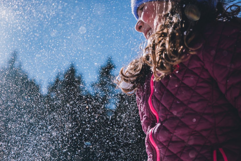 Smiling girl in a pink jacket with snow flying around her.