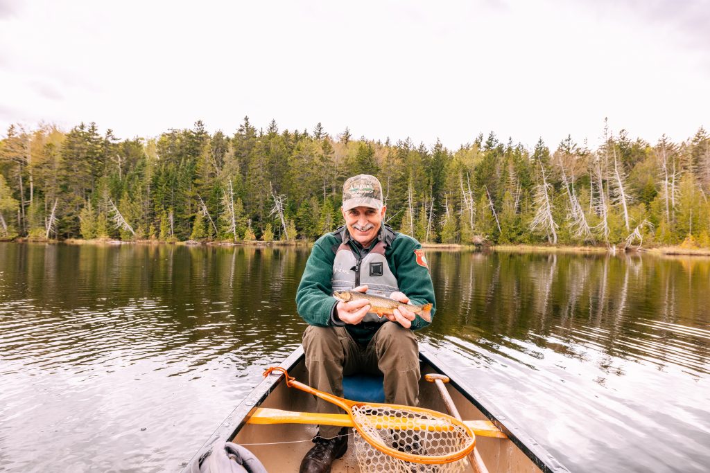Man holding a fish in the bow of a canoe.