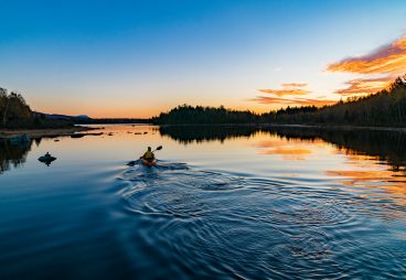 Paddlers at sunset under a blue and yellow sky.