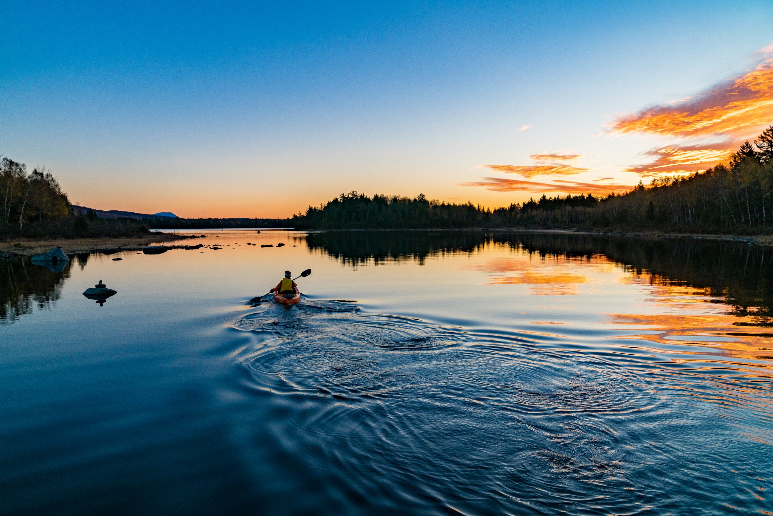 Paddlers at sunset under a blue and yellow sky.