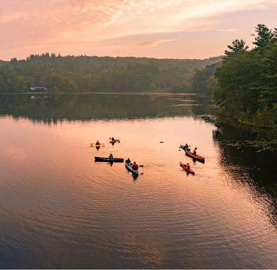 Page Header Mobile (2) aerial view of kayakers and canoes on pond at sunset