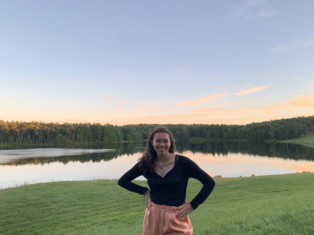 Woman smiling with hands on hips in front of a field and a pond.