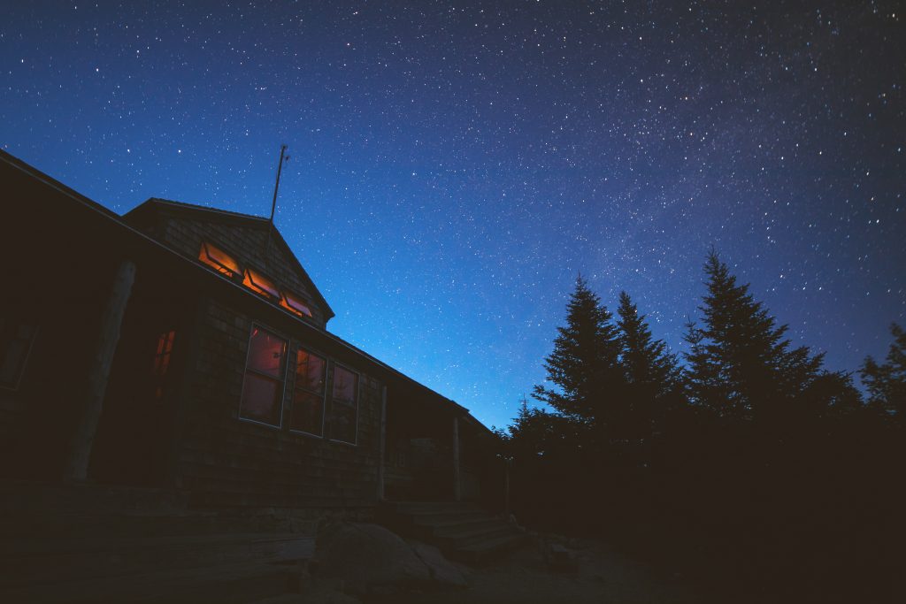 Zealand Falls Hut lit up from the inside with a twilight blue sky above.
