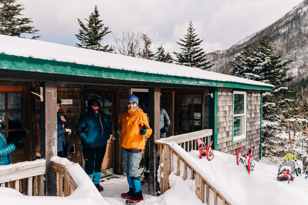 People smiling outside of Carter Notch Hut in winter.