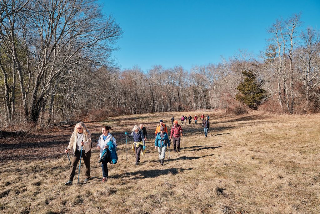 People walking on brown grassy trail in CT in winter.