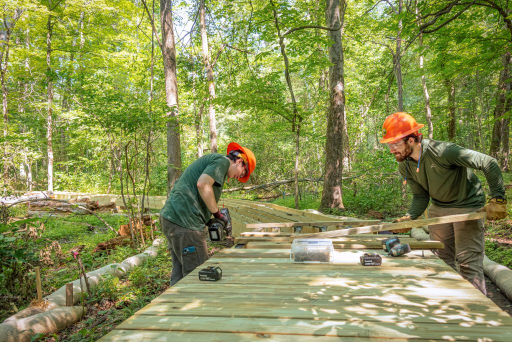 AMC trail crew with orange hard hats working on a wooden bridge.