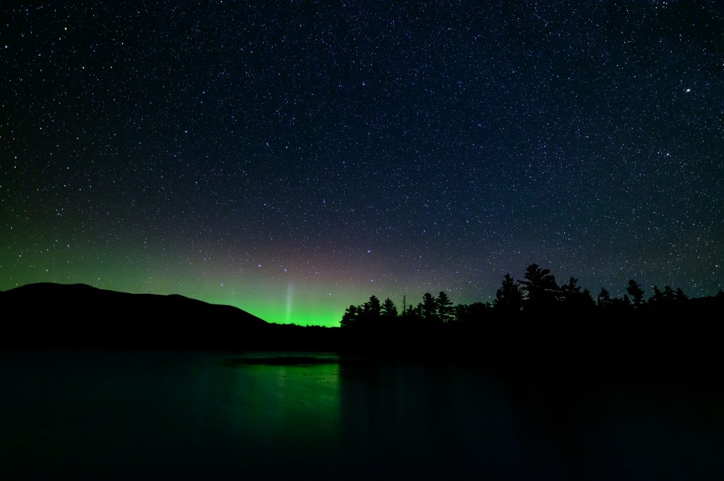 Northern lights over silhoutetted mountains and water.