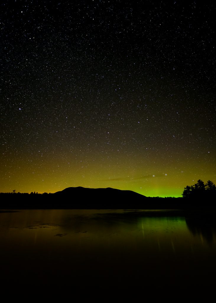 Yellow and green aurora over lake in the Maine Woods.