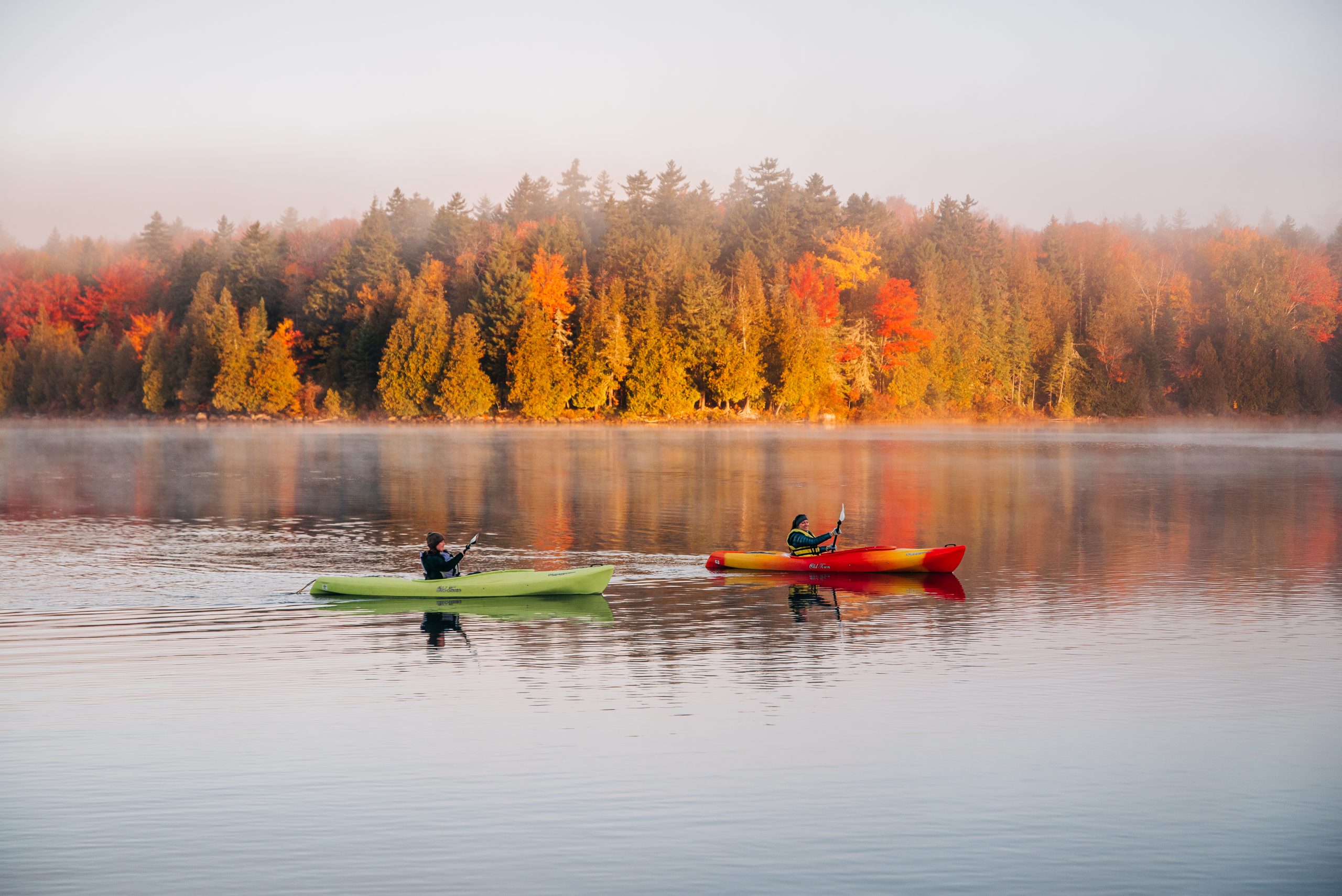 Two kayakers in front of fall foliage.