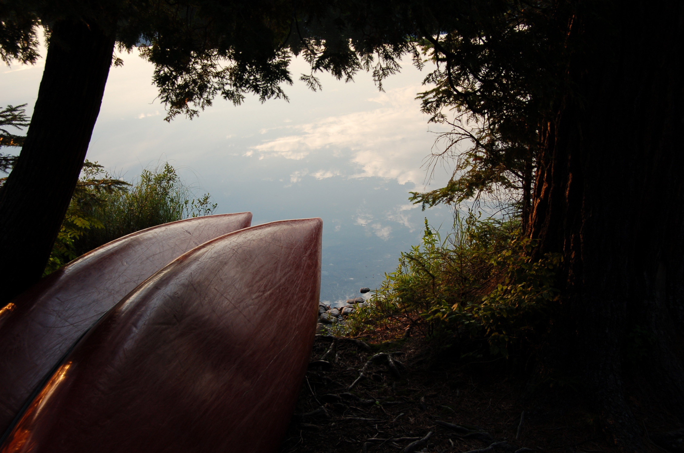 Two canoes on shore near a glassy lake.