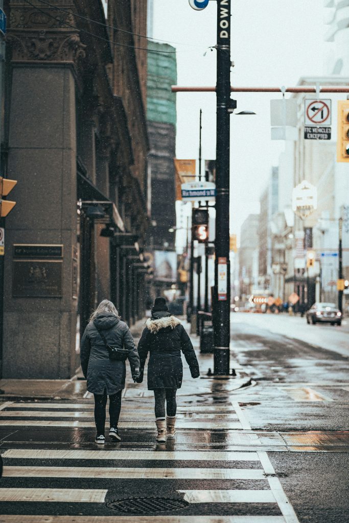 Two people in thick jackets walking in NYC and holding hands.