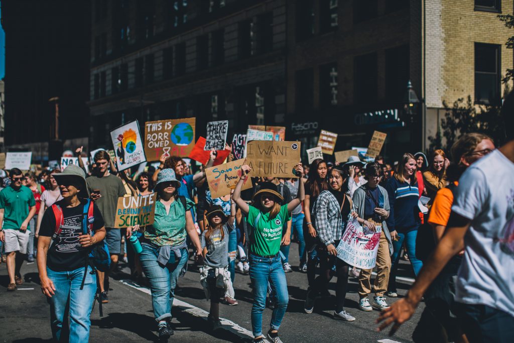 A group of people of all ages participate in the Boston Climate Strike, advocating for climate action with homemade signs. Signs read phrases like, "Unite Behind the Science" and "I Want a Future."