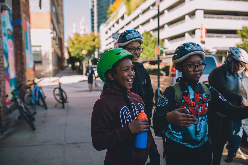 Four kids, still in helmets, take a break on a bike trip in Brooklyn, New York.