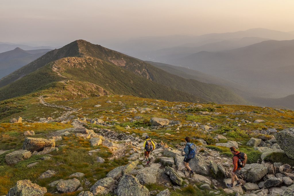 Three hikers on the Franconia trail with misty mountains in the background.