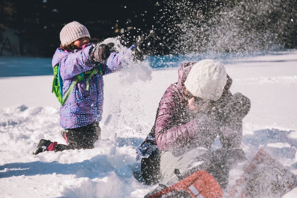 A kid dumps snow on an adult. Both are wearing snow gear and laughing.