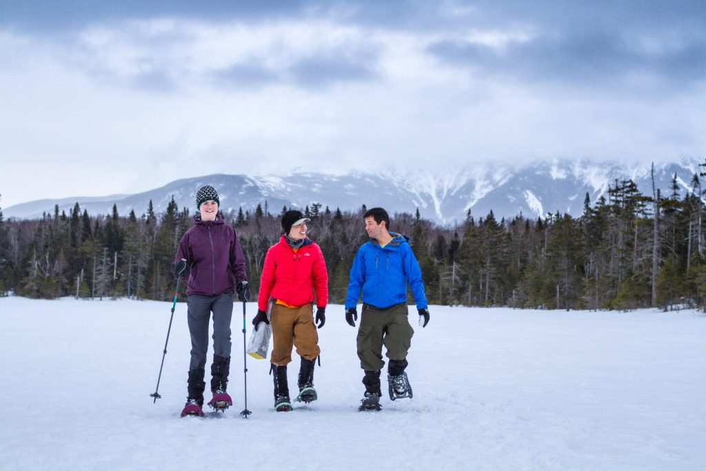 Three smiling people snowshoeing across a frozen lake.