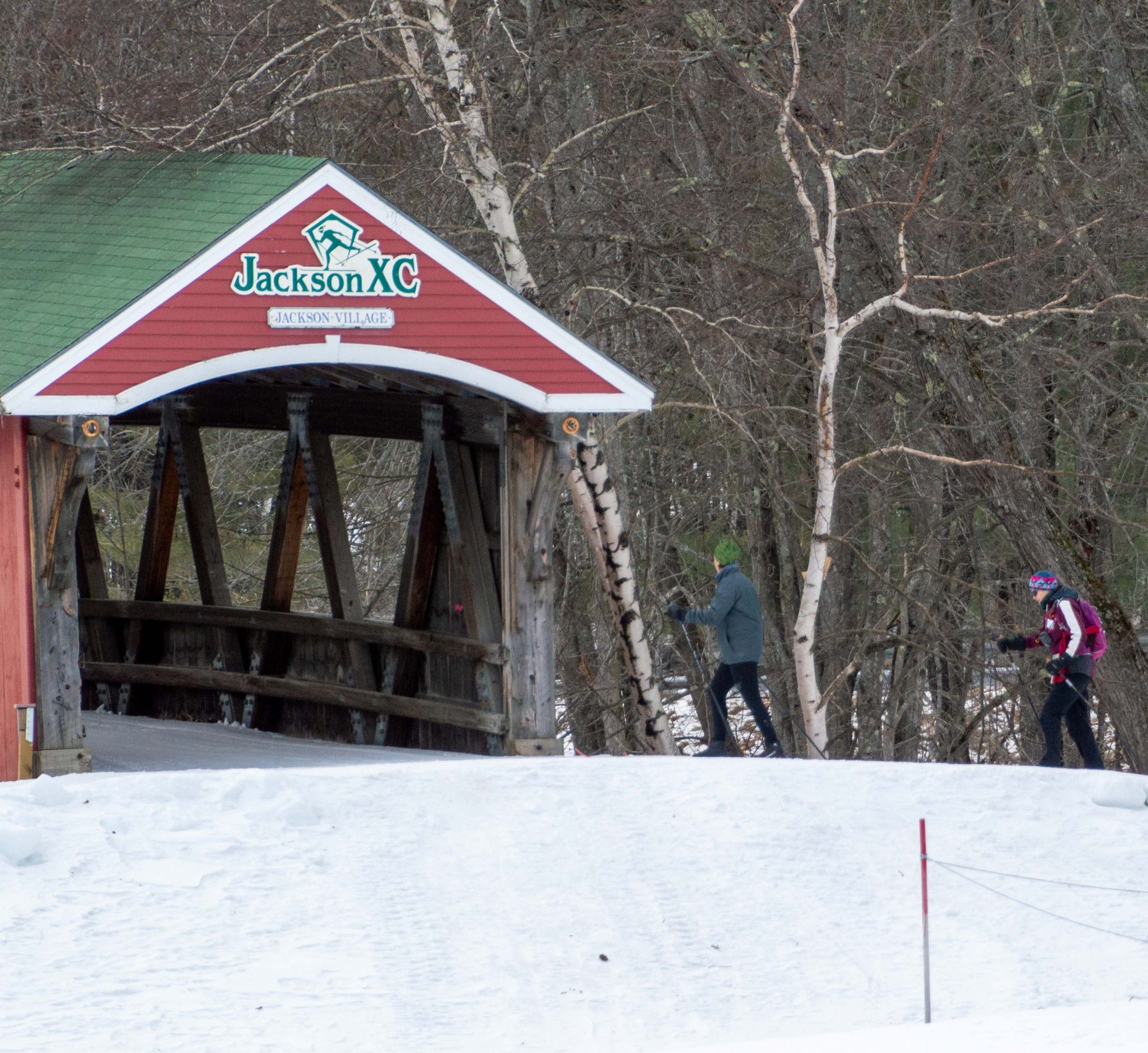 cross country skiiers about to cross a red covered bridge