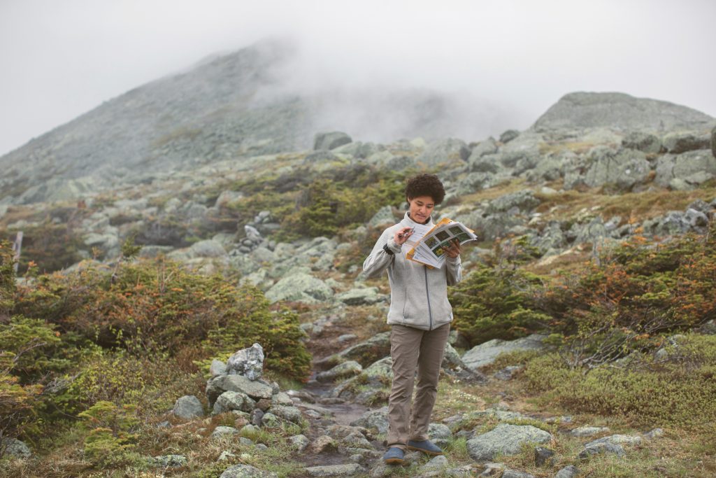 Amidst a rocky landscape and light fog, an AMC Naturalist takes notes on a stack of papers
