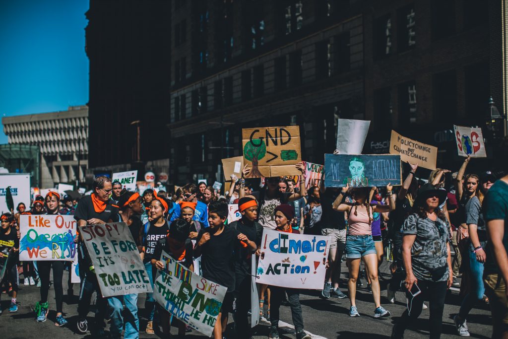A group of people of all ages march together in Boston, lifting up signs that support of climate action 