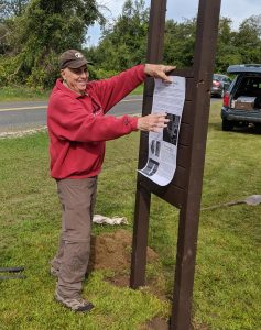 Steve Smith wears a red jacket as he hangs a sign on a brown signpost.