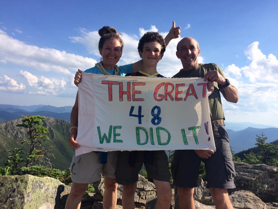 A family of three standing on top of Mt. Bond with a sign that says "THE GREAT 48 - WE DID IT!"