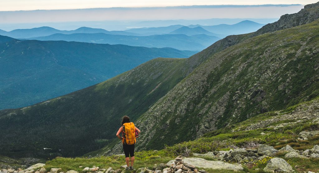 A young person with an orange backpack looks out at the mountains in the backyard.