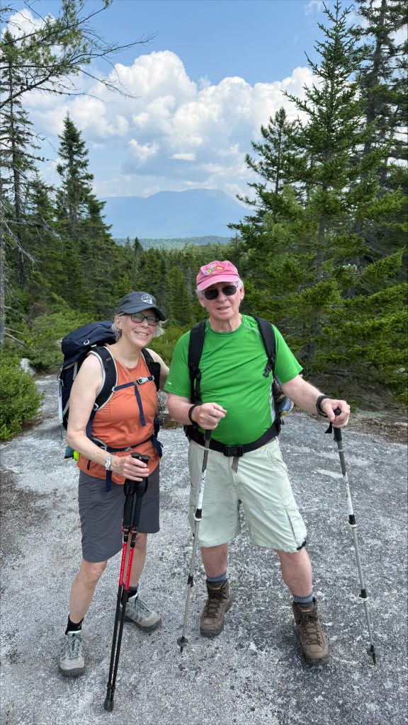 Ed and Marty wearing backpacks and standing on a granite slab surrounded by trees.