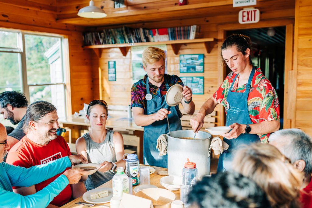 A colorfully-dressed Hut Croo serves soup to guests.