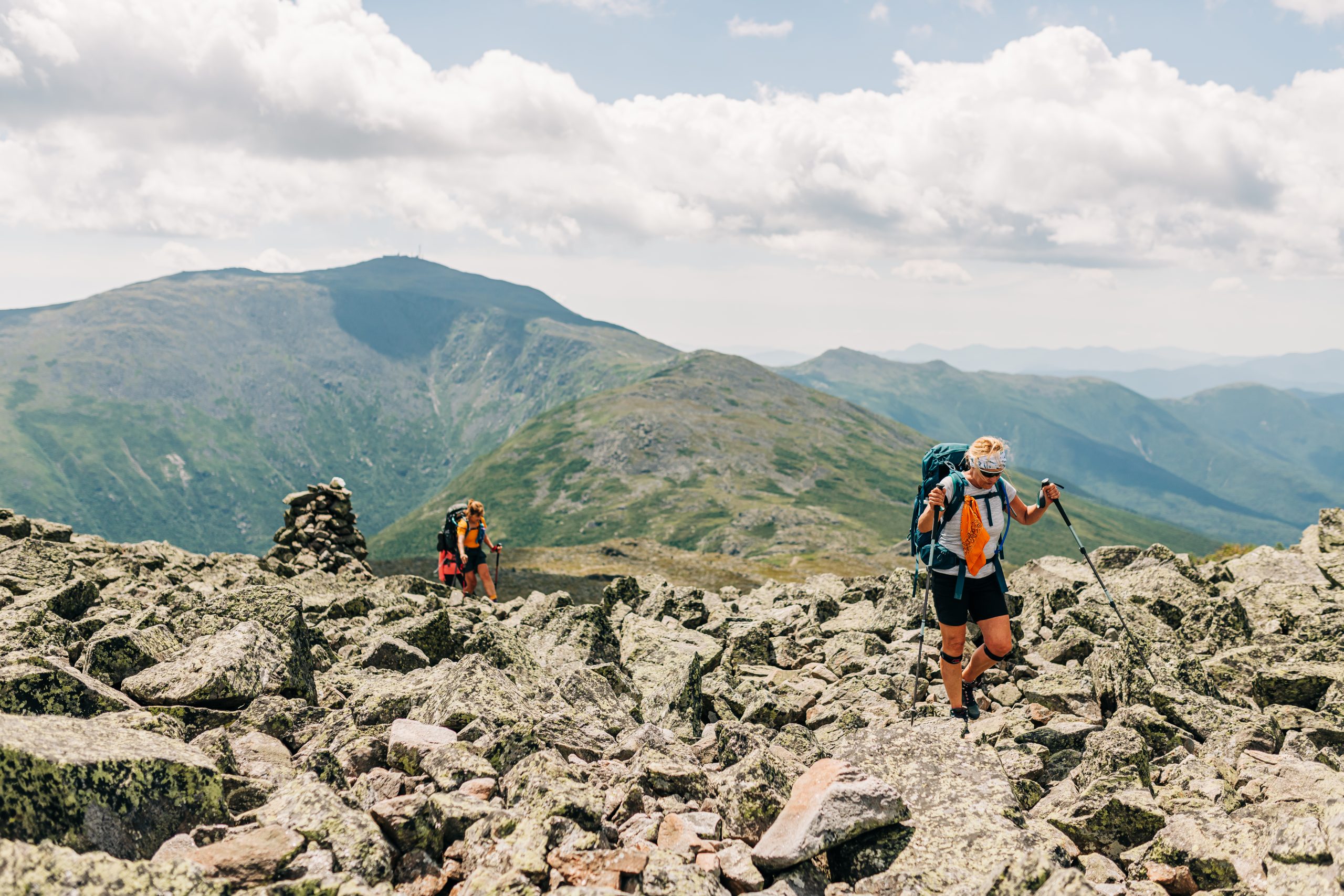 Hikers on a White Mountain ridge near a cairn.