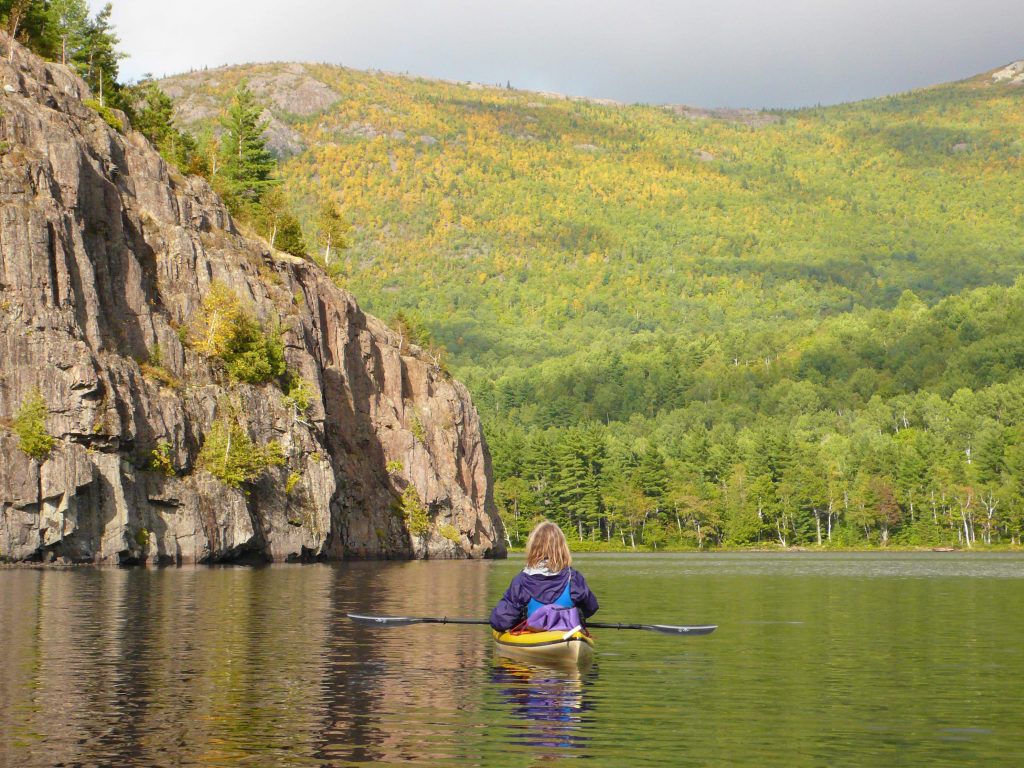 Person in purple jacket kayaks along a wide waterway with mountains in the background.