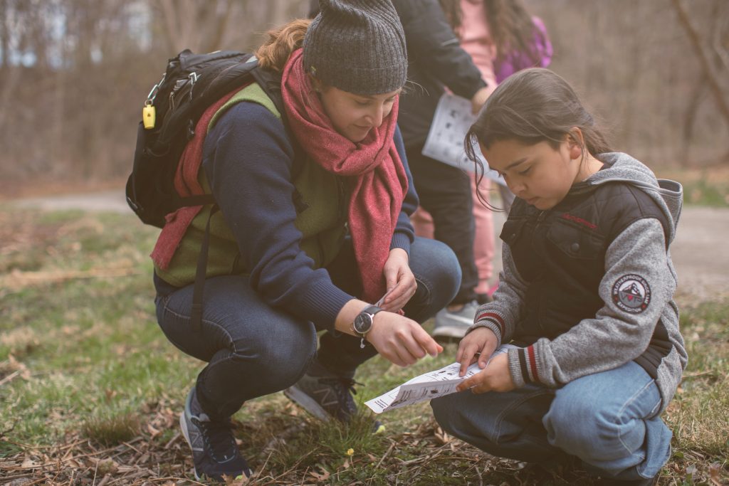 A naturalist squats next to a child and points out something on a piece of paper.