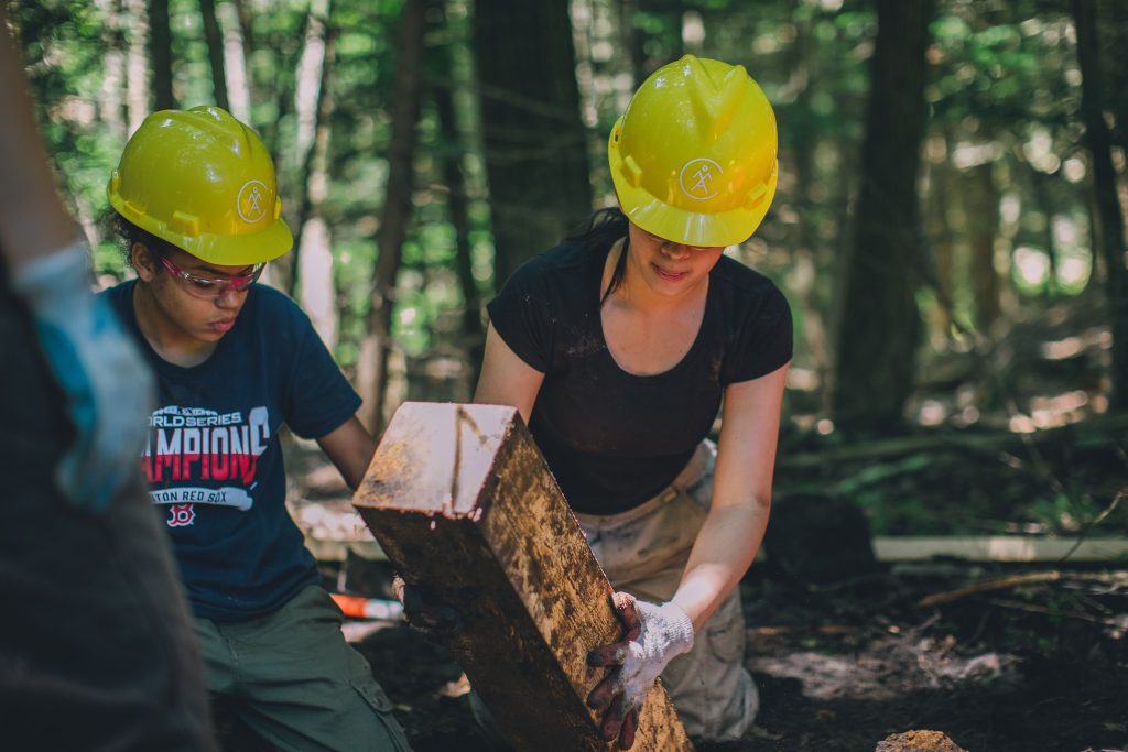 Two volunteers wearing hard hats work on a trail.