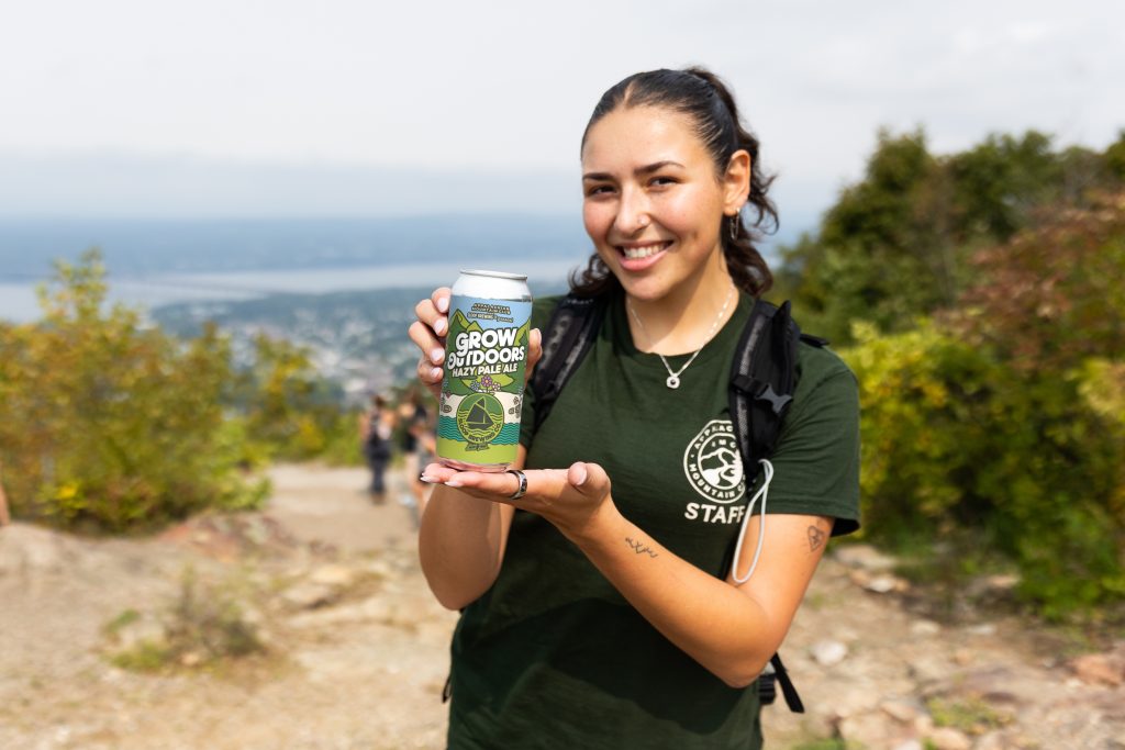 a person in an AMC shirt holding Grow Outdoors beer can